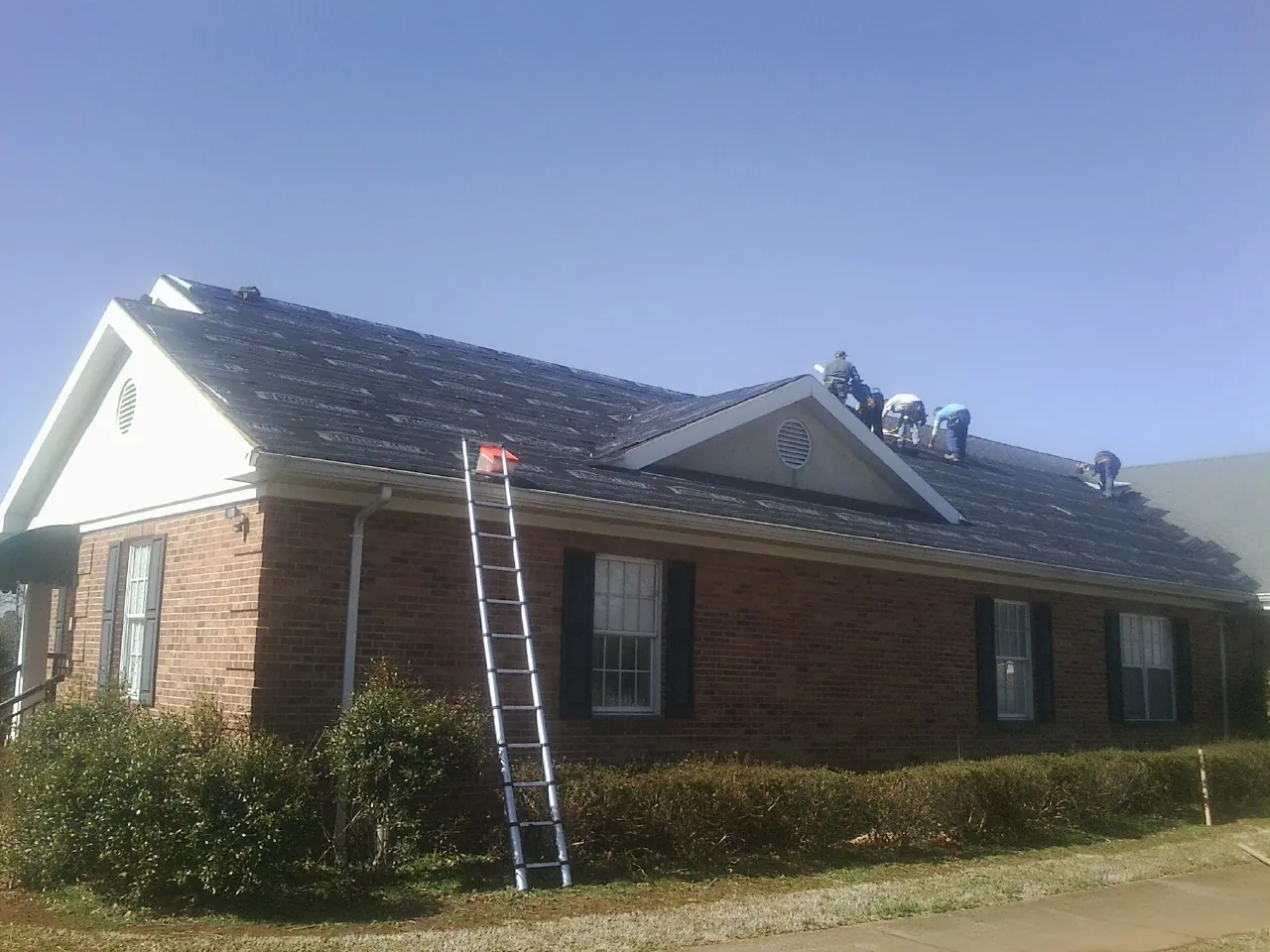 Crew tearing shingles off a brick ranch roof with a ladder set — Emergency Roof Repair work by our crew in Valencia