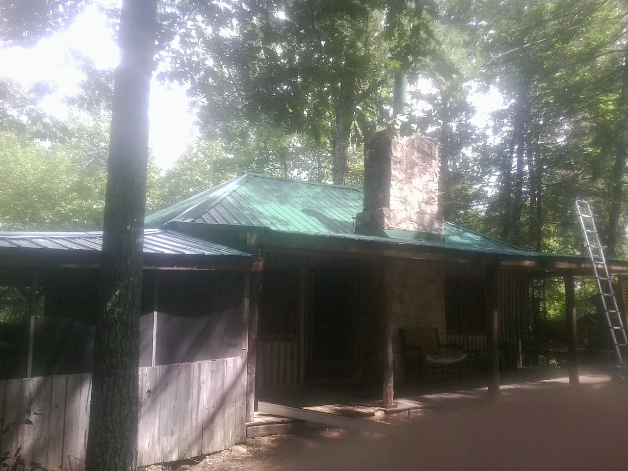Green metal roof and stone chimney above a log cabin porch in Valencia