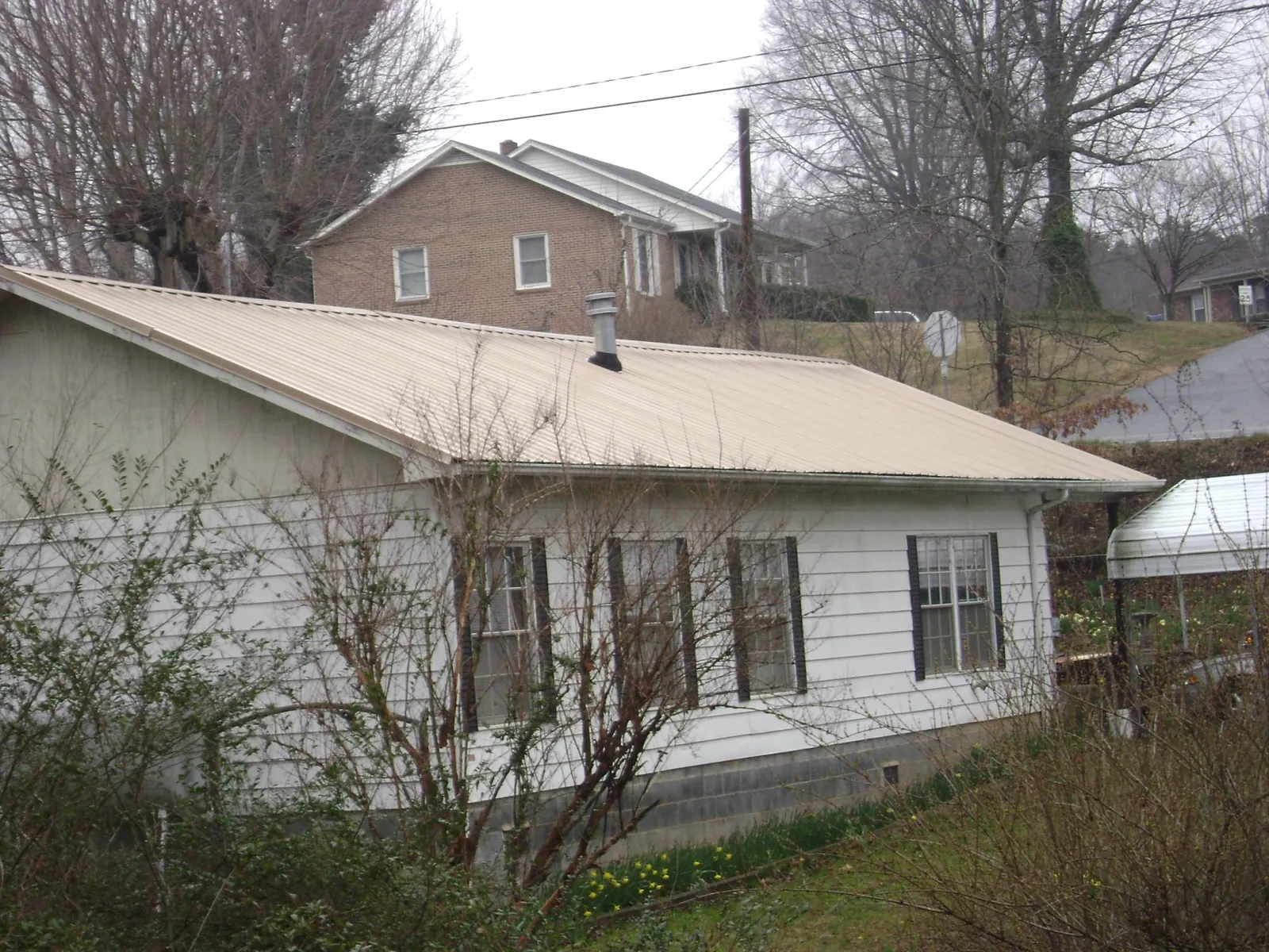 Tan metal roof on a white sided house set into a hillside — Commercial Roofing by Roofing Brothers in Valencia